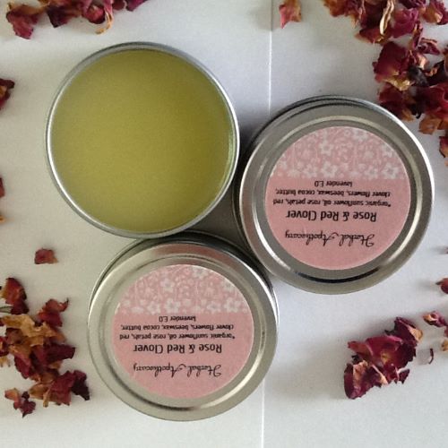 A cluster of Rose & Red Clover salves with rose petals strewn all around